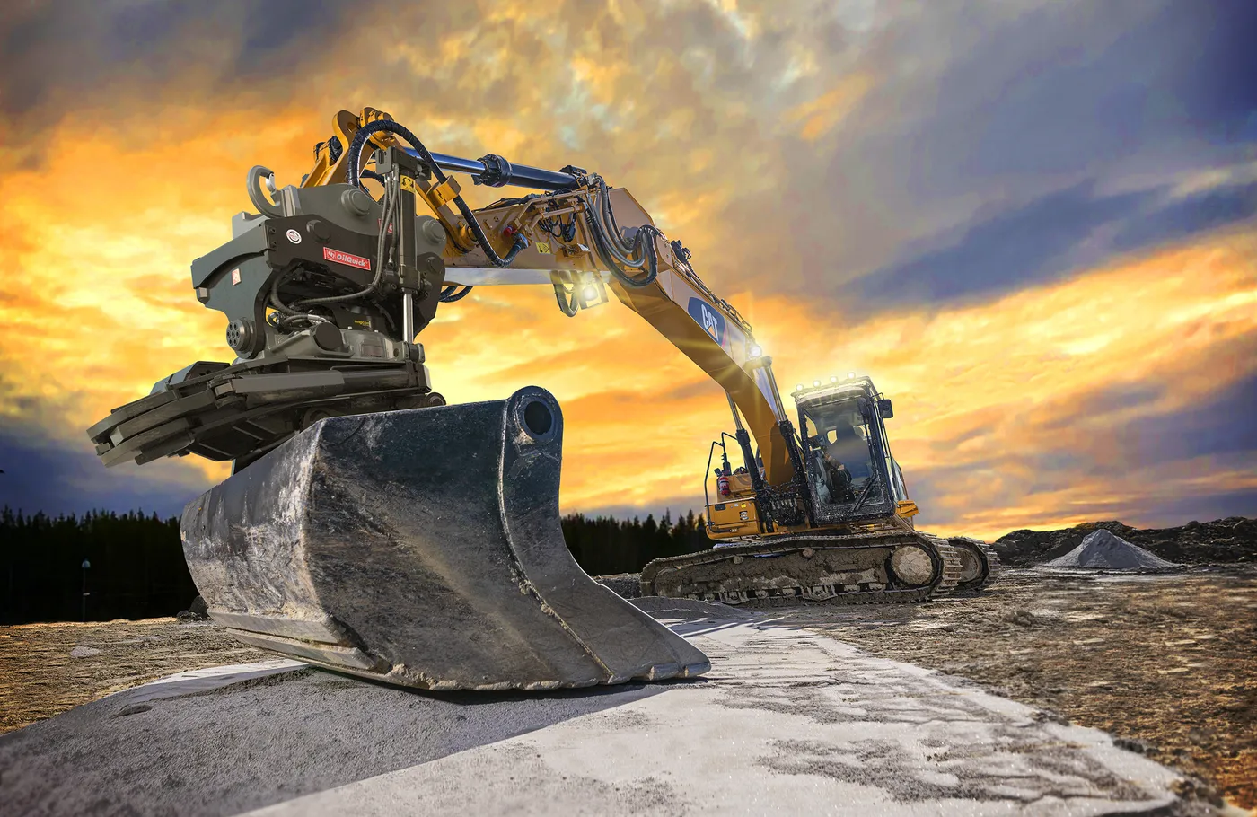 Excavator fitted with an OilQuick OQTR-E tiltrotator tilting a bucket at sunset